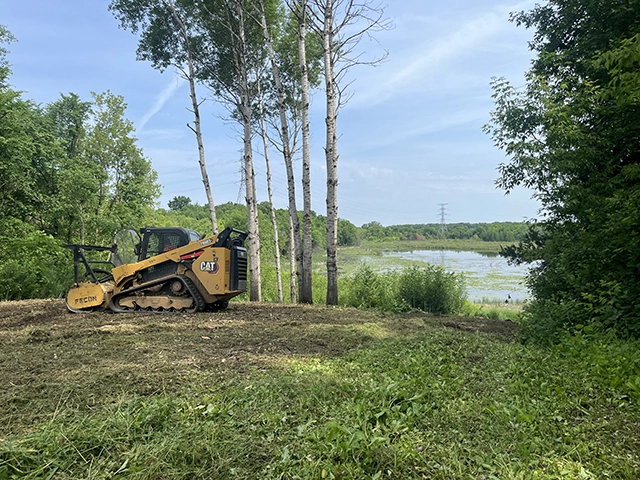 A bobcat with land clearing attachment on a recently cleared hill.