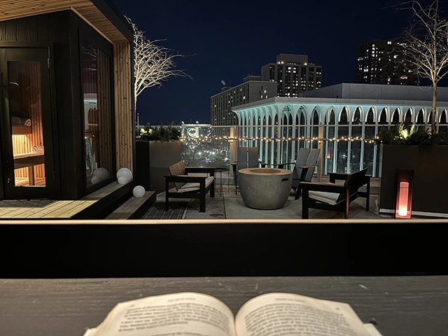 Behind a desk at a rooftop terrace looking out at a city skyline at night.